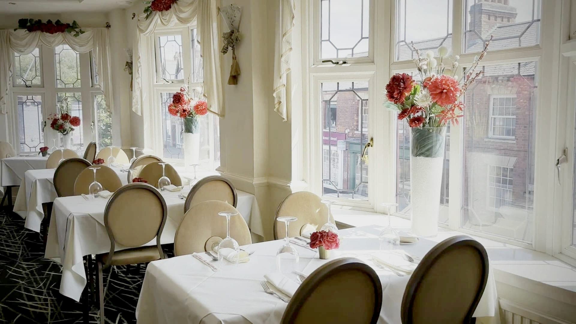 The dining room in daylight, tables laid with white linen beneath the tall leaded bay windows